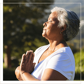 mature woman of Hispanic descent standing in prayer pose facing the sun with her eyes closed as she prays and contemplates mobile version