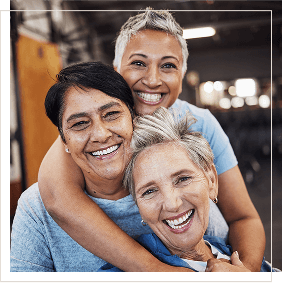 three mature women of different ethnicities smiling and holding each other with tenderness mobile version
