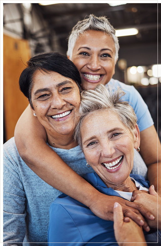 three mature women of different ethnicities smiling and holding each other with tenderness